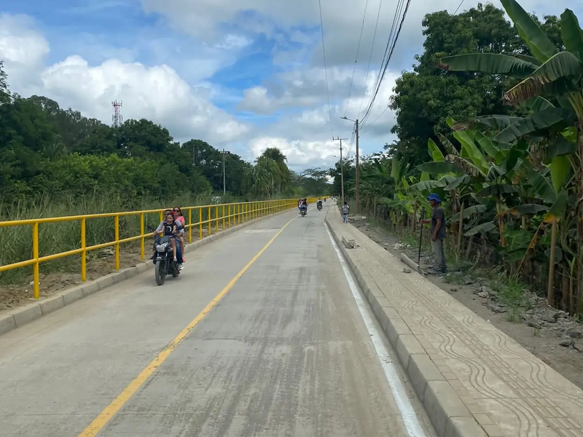 Vía en placa de concreto terminada en la vereda Santa Rosa, con barandas amarillas y motociclistas circulando