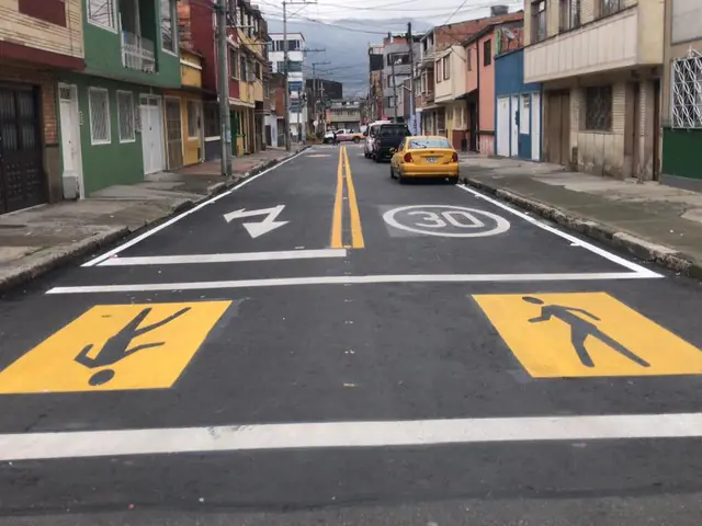 Calle con senda peatonal amarilla y límite de velocidad pintados sobre el asfalto