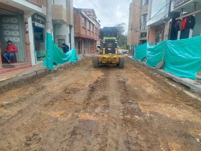 Maquinaria conformando la base de la calzada entre cerramientos verdes